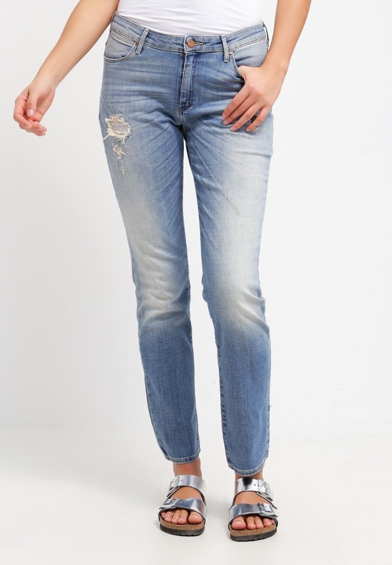 Vaaleansiniset farkut, joissa on haalistuneita kohtia ja kuluneita yksityiskohtia, suora malli ja neljä taskua, yhdistettynä hopeisiin sandaaleihin.