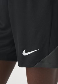 Svartidrettsshorts laget av teksturert stoff, med en hvit Nike-logo på kanten og en lysere grå aksent på siden.