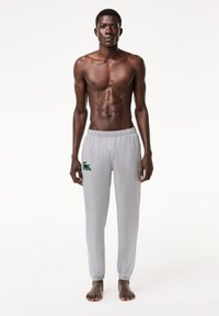 Grå bomullssvetterbukser med elastisk liv og mansjetter, med en grønn Lacoste-logo på venstre side, glatt tekstur og avslappet passform.