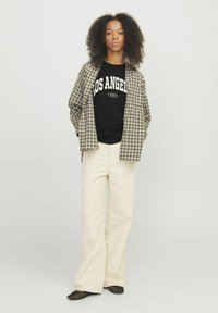 Camicia a quadri beige e marrone sopra una t-shirt nera con la scritta "LOS ANGELES". Pantaloni ampi crema e ballerine nere in rete.