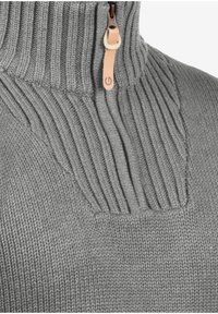 Grijze gebreide trui met hoge kraag, voorzien van ribbelstructuur en een ritssluiting. Verfraaid met een leren trekkoord.