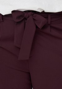 Burgundy high-waisted pants with a tied bow detail at the waist, made of smooth fabric, featuring flat front and side pockets.