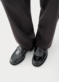 Svarte lærloafers med en glatt finish, dekorative sømmer og et lavprofildesign, kombinert med mørke bukser.