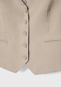 Gilet beige à boutons avec cinq boutons et deux poches horizontales fentes de chaque côté, coupe ajustée avec ourlet pointu.