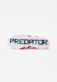 Semelle de chaussure de football rouge et blanche avec un motif texturé ; "PREDATOR" en lettres noires en gras sur le dessous ; semelle extérieure transparente.