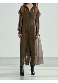 Lång, genomskinlig brun klänning med krage, broderade detaljer fram och ballongärmar. Bärs över åtsittande, svarta anklar boots.