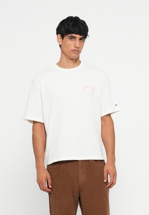 Hvid bomulds t-shirt med korte ærmer, udført med et lille orange logo på venstre bryst. Løs pasform, rund halsudskæring, subtil tekstureret finish.