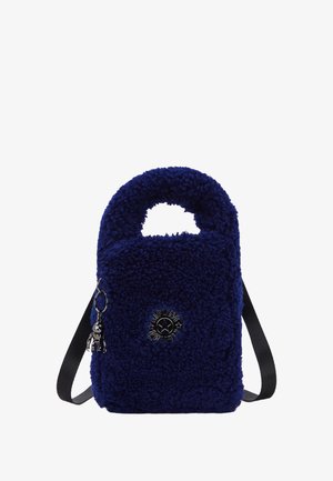 Pequeño bolso de mano azul marino de peluche con un asa superior, una correa para el hombro ajustable negra y un logo metálico redondo con un charm de llavero.
