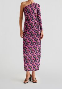 Robe longue asymétrique en motif ondulé rose, violet et noir, confectionnée dans un tissu texturé avec un détail froncé sur le côté.