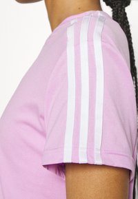 Camiseta de algodón de manga corta en color rosa, con tres franjas blancas en el hombro para un contraste. Textura suave.