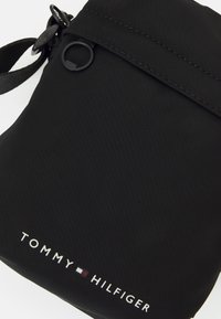 Borsa a tracolla nera in nylon con chiusura a zip, tracolla regolabile e logo stampato, caratterizzata da una texture liscia e un design minimalista.