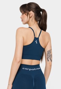 Jūras spēku sporta krūšturis ar plānām siksnām un logotipa akcentu. Iezīmēts ar pieguļošu dizainu un teksturētu audumu. Modelis pozē ar muguru pret kameru, demonstrējot krūšturi.