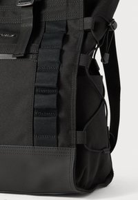 Zaino nero con un esterno texturizzato, dotato di spallacci regolabili, più tasche laterali e un pannello inferiore impermeabile per maggiore durata.