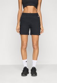 Svarta cargo shorts med elastisk midja, sidofickor och logopatch; kombinerat med svarta sneakers och vita crew-strumpor med logga.