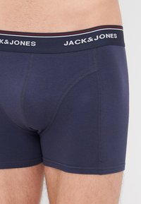 Tamno plave bokserice s uskim fitom, s kontrastnom elastičnom pojasom na kojem se nalazi natpis "JACK & JONES" i dekorativnim trakama.