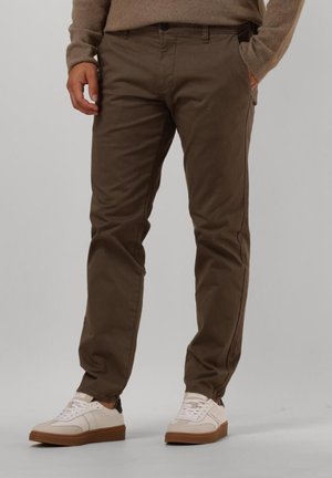 Brune bomulds-chinos med slim-fit design, forlommer og en glat texture, parret med hvide sneakers med brune detaljer.