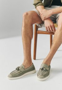 Lys grå slip-on sko med vævede accenter, fringing detalje og en hvid gummisål, der har en glat læderoverflade.
