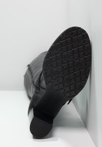 Musta nahkasaapas, jossa on teksturoitu pinta ja matala lohkoiltapäkä. Varustettu kuvioidulla kumipohjalla pidon lisäämiseksi. Sivuvetoketju näkyvissä.