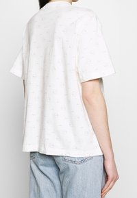 Bílé bavlněné tričko s krátkými rukávy, zdobené jemným celoplošným potiskem kruhů a log Nike. Pohodlný střih a uvolněná silueta.