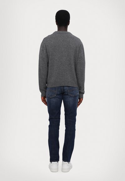 Grau gestrickter Pullover mit Rundhalsausschnitt, getragen mit dunkelblauen Jeans und weißen Sneakers, von hinten gezeigt.