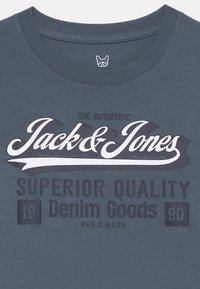 T-shirt en coton bleu avec un col rond et un impression de texte noir et blanc audacieuse : "Les Vrais Produits en Denim de Qualité Supérieure Jack & Jones."