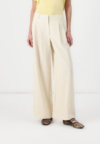 Beige wide-leg trousers made of lightweight fabric with pleats, paired with black and brown leopard-print flats, creating a contrasting look.