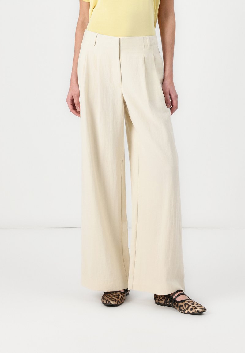Beige wide-leg trousers made of lightweight fabric with pleats, paired with black and brown leopard-print flats, creating a contrasting look.