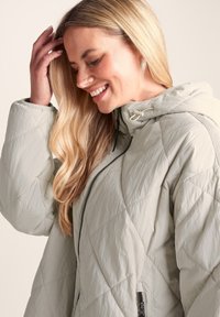 Quilted light grey jacket with a hood, featuring horizontal and diamond patterns, front zipper, and adjustable drawstring details.