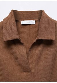 Polo shirt texturé marron avec un col et un design en forme de V. Étiquette visible à l'intérieur du col, indiquant le nom de la marque.