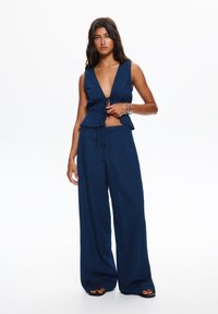 Marineblauw linnenoutfit met een cropped, mouwloos topje met een diepe V-hals en een peplum taille, gecombineerd met een breed uitgesneden broek.