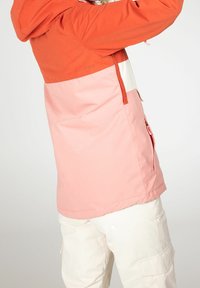 Persona con una chaqueta de bloques de color en naranja, rosa y blanco, con un bolsillo lateral con cierre, combinada con pantalones cargo blancos.