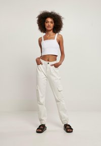 Hvit avkortet tank top med firkantet hals; løstsittende, lyse cargo-bukser med lommer; sorte slip-on sandaler.