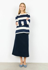 Tumeroheline ja valge triibuline pikkade varrukatega pusa ümarate kaelustega, kombineeritud tekstuurse tumerohelise pika seelikuga ja heleroheliste kontsakingadega.