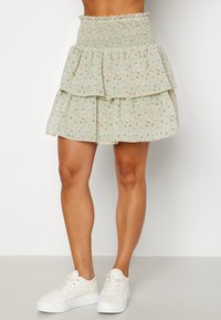 Jupe verte à volants avec imprimé floral, taille smockée et tissu léger. Associée à des baskets blanches pour un look décontracté.