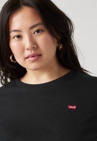 Black t-shirt with a round neckline, featuring a small red Levi's logo patch on the chest and a smooth, cotton texture.