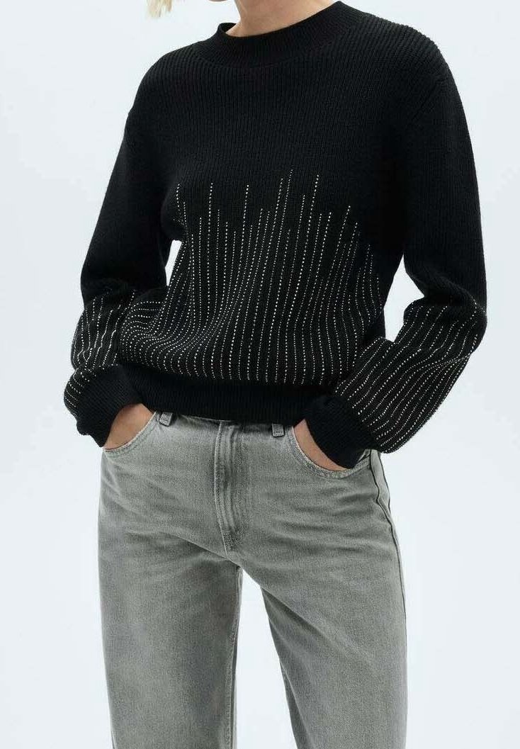 Schwarzer Strickpullover mit Rippentextur, verziert mit silberfarbenen metallischen Details in vertikalen Linien, kombiniert mit hellgrauen Jeans.