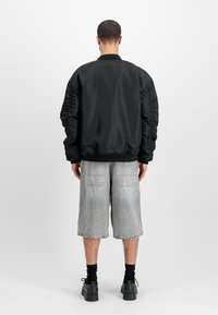 Black bomber jacket with textured puffed sleeves, ribbed collar, and cuffs. Paired with light grey denim shorts and black shoes.