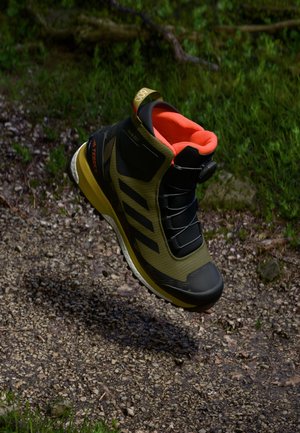 Olive green hiking boot with black accents, a high-top design, orange interior, and textured sole, featuring a speed lacing system.