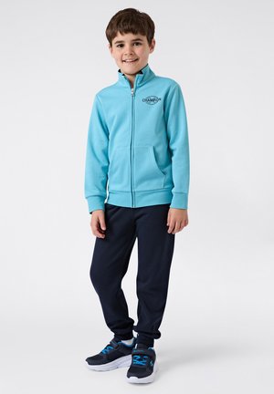 Lichtblauwe zip-up hoodie met voorzakken, marineblauwe sweatpants en zwarte sneakers met blauwe accenten. Eenvoudige, jeugdige sportkleding.
