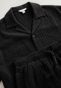 Sort tekstureret bomulds-pyjamasæt med skjorte med knapper og krave samt bukser med elastik i taljen og snøre, størrelse medium.