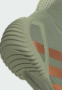 Primer plano de la suela de un zapato deportivo verde con agarre texturizado y rayas naranjas en la sección superior de tejido de punto.