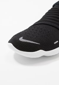Chaussure de sport noire avec une tige en tricot texturé, une semelle en caoutchouc blanche et un logo Swoosh argenté sur le côté.