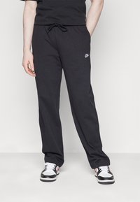 Černé tepláky vyrobené z měkké látky, s elastickým pasem na šňůrku a malým bílým logem Nike na levém stehně.