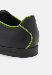 Černá kožená bota s kontrastním neonově zeleným prošitím, mírně zakřiveným zadním dílem a gumovou podrážkou s embosovaným nápisem "Emporio Armani."