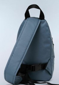 Sac à dos en tissu bleu avec un design élégant et angulaire. Doté d'une sangle noire et d'une boucle, d'une texture lisse et de lignes minimalistes.