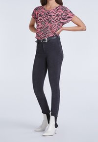 Haut à manches courtes rayé zèbre rose et noir, associé à un jean skinny noir taille haute et des bottines blanches avec des accents noirs.