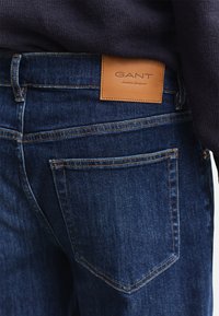 Σκούρο μπλε τζιν από denim με ταμπά δερμάτινη ετικέτα GANT στη πίσω μέση, φορεμένα με σκούτερο πουλόβερ με υφή.