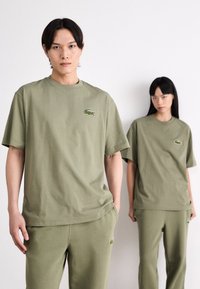 Olijfgroene katoenen oversized t-shirts en bijpassende sweatpants, met geborduurde logo-accenten op de borst en dij.