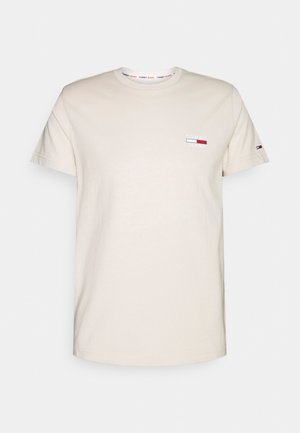 Beżowy t-shirt z krótkim rękawem i okrągłym dekoltem z małym logo Tommy Jeans na piersi i rękawie, jednolite tło.