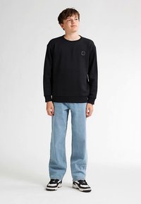 Zwarte sweatshirt van katoen met een ronde hals, geribde manchetten en een klein cirkelvormig logo op de borst, gecombineerd met lichtblauwe spijkerbroek en sneakers.